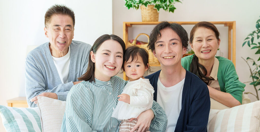 明るいリビングのソファに集まって笑顔を見せる3世代家族と赤ちゃん
